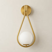 Brass teardrop wall sconce with a round white glass globe on a light gray wall.