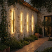 Four warm vertical outdoor wall lights mounted on a rustic stone garden wall.