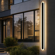 Tall rounded rectangular wall light glowing beside a modern home exterior.