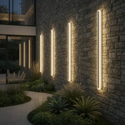 Warm vertical tube lights mounted on a stone exterior wall beside landscaped plants.