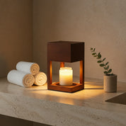 Glowing candle lantern on a stone counter with rolled towels and a small potted plant.