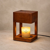 Wooden cube candle warmer with a glowing frosted glass candle on a neutral tabletop.