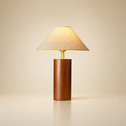 Wooden table lamp with beige fabric shade and brass neck on a plain warm background.