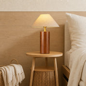 Wooden cylindrical table lamp with a beige fabric shade glowing on a bedside table.