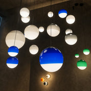 Glossy spherical pendant lights in blue, green, and white hang against a dark wall.
