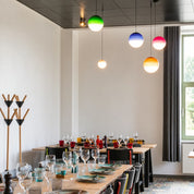 Colorful spherical pendant lights hang above a long dining table set with glassware and plates.