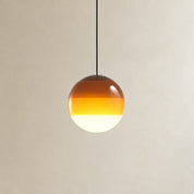 Amber gradient glass globe pendant light hanging from a black cord against a pale wall.