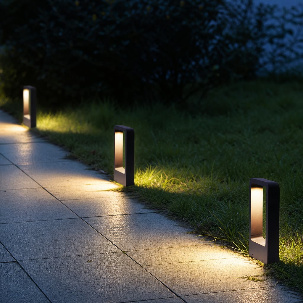 Three black rectangular pathway lights illuminate a tiled garden walkway at dusk.