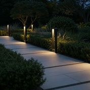 Black rectangular bollard lights illuminate a tiled garden walkway at dusk.