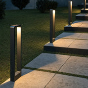 Black rectangular pathway bollard lights illuminate stone steps in a grassy garden.