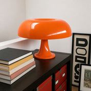 Glossy orange mushroom table lamp on a dark cabinet beside stacked books.