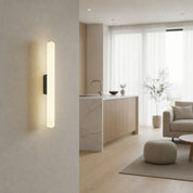 Warm vertical wall sconce on a beige wall in a softly lit modern living space.