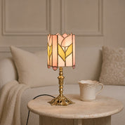 Tulip stained glass table lamp with ornate brass base on a round stone table.