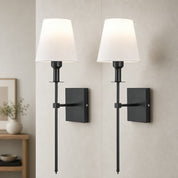 Two black wall sconces with white fabric shades mounted on a light gray wall.