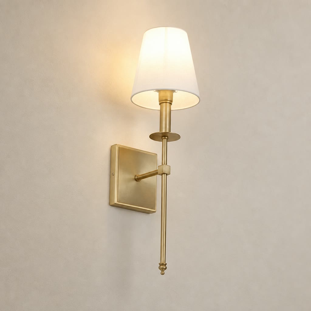 Brass wall sconce with a glowing cream shade on a plain light gray wall.