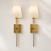 Pair of brass wall sconces with cream fabric shades and rectangular backplates on a pale wall.