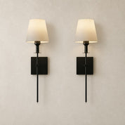 Pair of black wall sconces with cream fabric shades on a pale neutral wall.