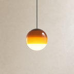 Amber gradient glass globe pendant light hanging from a black cord against a pale wall.