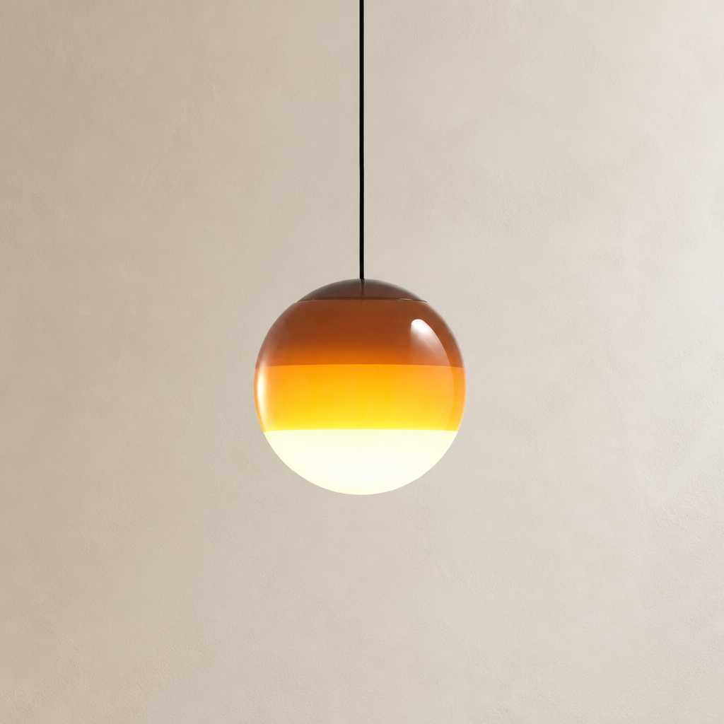Amber gradient glass globe pendant light hanging from a black cord against a pale wall.