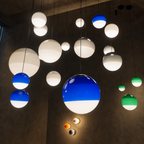 Glossy spherical pendant lights in blue, green, and white hang against a dark wall.