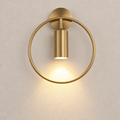 Brushed gold circular wall sconce with a glowing downward cylinder light on a pale wall.