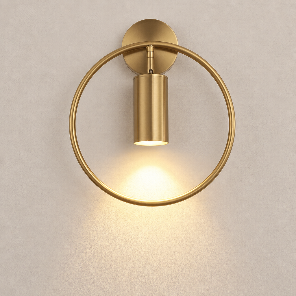 Brushed gold circular wall sconce with a glowing downward cylinder light on a pale wall.
