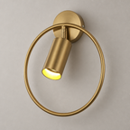 Brass circular wall sconce with a tilted lit cylinder shade on a plain wall.