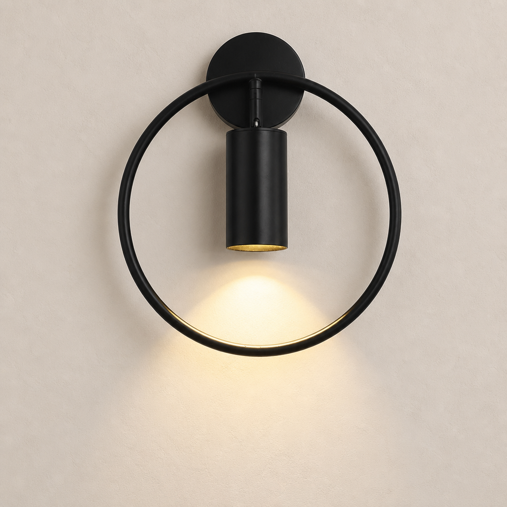 Black circular wall sconce with a cylindrical downlight casting a warm glow on a pale wall.