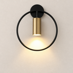 Black and brass circular wall sconce casting warm light on a pale wall.