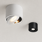 White and black cylindrical ceiling spotlights with warm recessed lights on a pale textured ceiling.