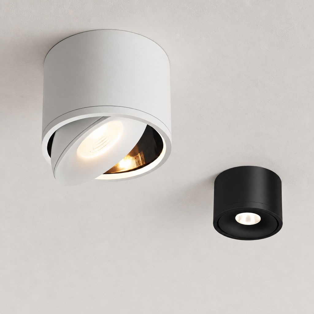 White and black cylindrical ceiling spotlights with warm recessed lights on a pale textured ceiling.