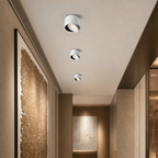 Three white cylindrical adjustable spotlights mounted along a modern hallway ceiling.