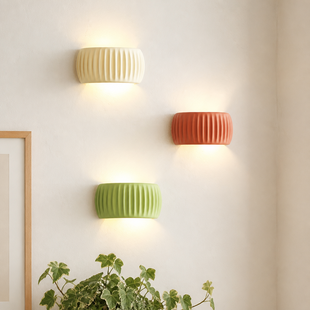Three ribbed ceramic wall lights in cream, coral, and green glow on a white wall.