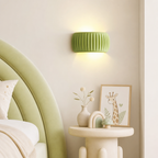 Lime green ribbed wall sconce glowing above a pastel bedside table in a soft bedroom.