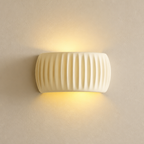 Cream ribbed resin wall sconce glowing warmly on a pale textured wall.