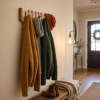 Wooden wall hooks hold a mustard cardigan, gray scarf, green quilted jacket, and orange knit beanie.