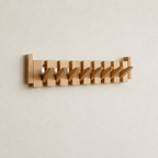 Wooden wall-mounted coat rack with angled pegs on a pale wall.