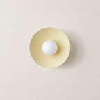 Cream circular wall sconce with a centered white globe bulb on a neutral wall.