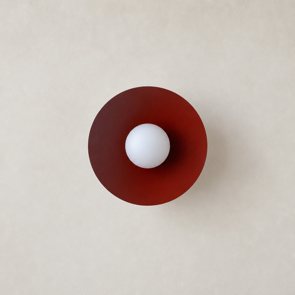 Burgundy circular lamp shade with a central white globe on a warm neutral wall.