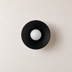 Black circular wall sconce with a white spherical bulb centered on a pale wall.