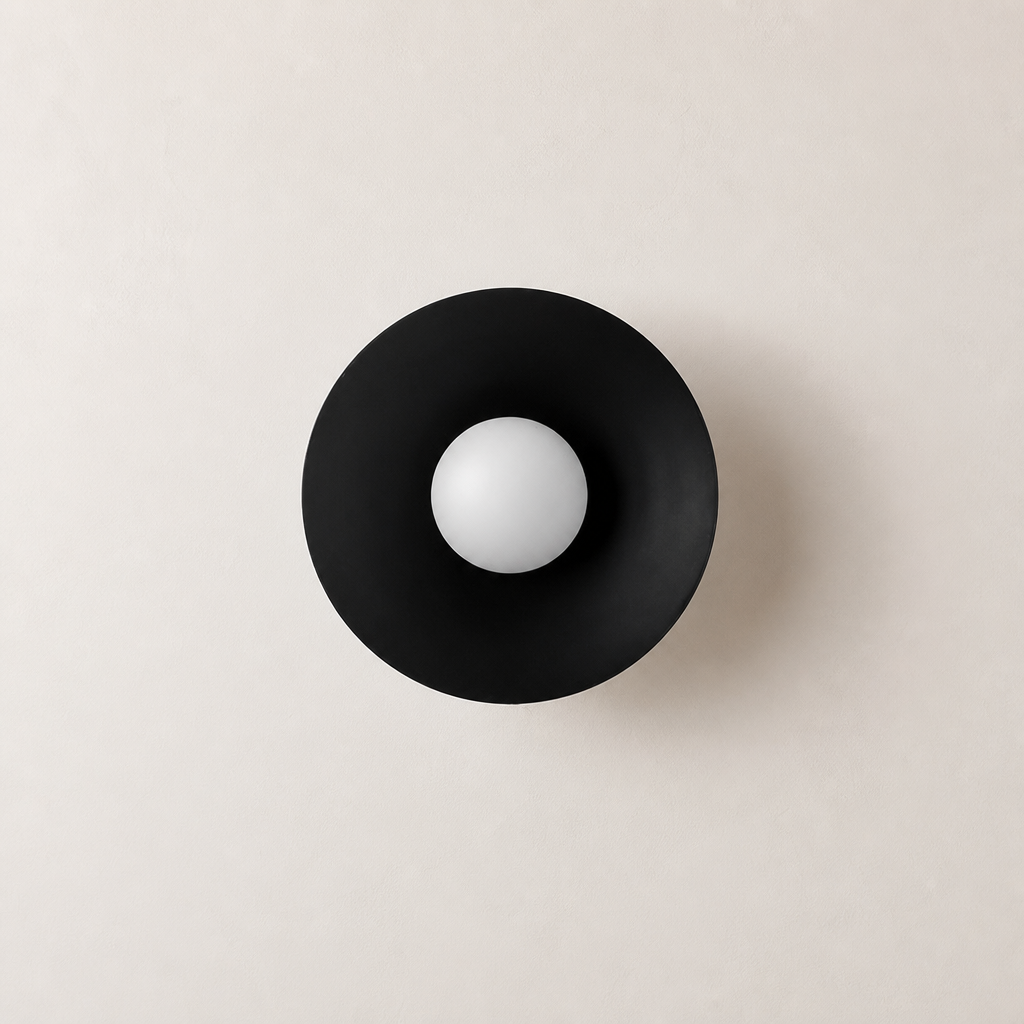 Black circular wall sconce with a white spherical bulb centered on a pale wall.