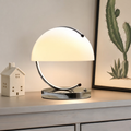 Glowing dome table lamp with chrome circular frame on a light wooden shelf.