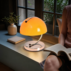 Glowing orange dome table lamp with chrome curved stem on a window bench.