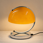 Glossy orange dome table lamp with chrome loop frame, oval base, and black power cord.