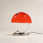 Glossy red dome table lamp with chrome curved stem and base on a neutral background.