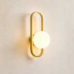 Gold oval wall sconce with a glowing round white globe on a light textured wall.