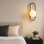 Black oval wall sconce with glowing frosted globe above a bedside table.