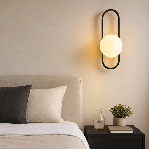 Black oval wall sconce with glowing frosted globe above a bedside table.