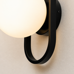 Glowing frosted globe wall sconce with black circular metal bracket on a pale textured wall.
