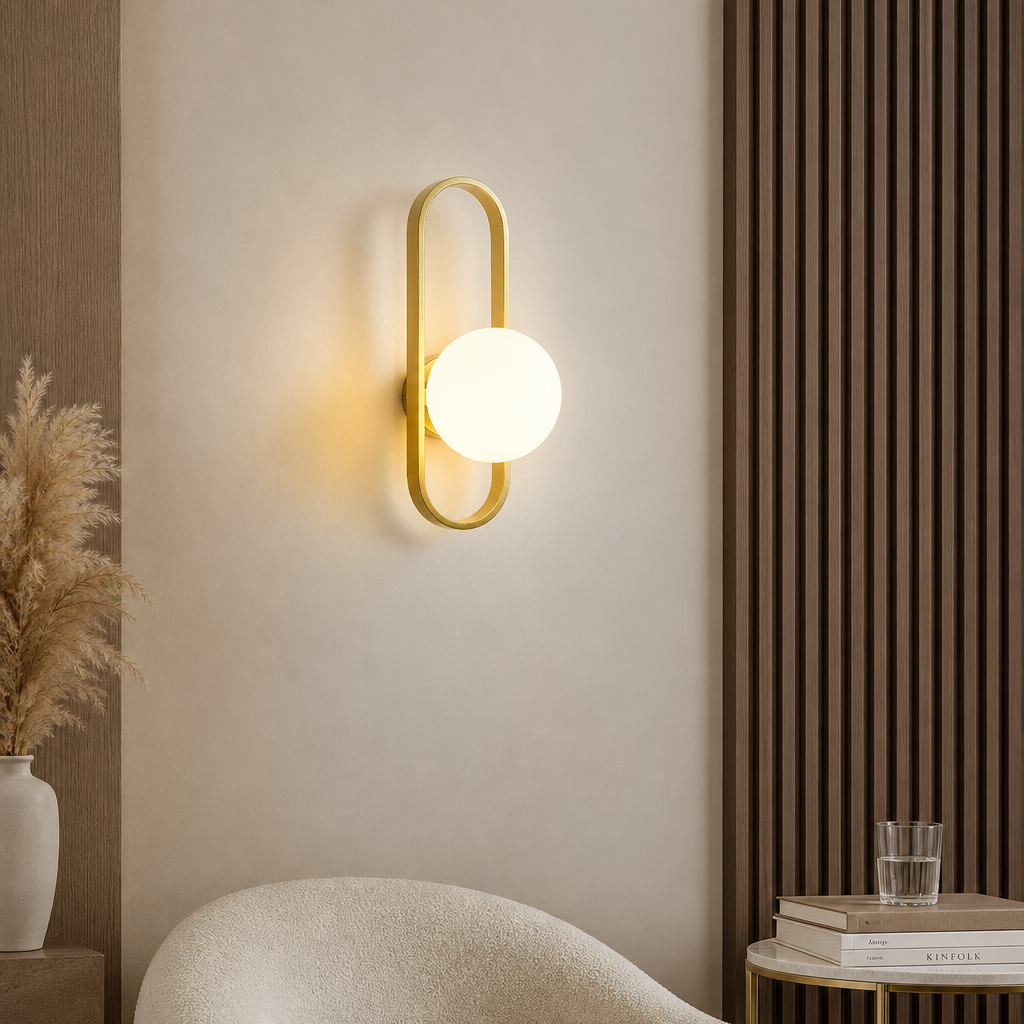 Gold oval wall sconce with a glowing white globe mounted on a warm neutral wall.